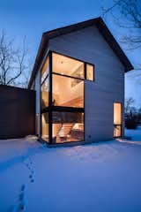 Exterior, Flat RoofLine, House Building Type, Wood Siding Material, and Gable RoofLine Large-scale picture windows help bring as much natural light into the home as possible.  Photos from An Intern Architect Builds a Home For His Growing Family on a Strict Budget
