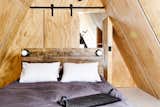 Bedroom, Wall Lighting, Bed, and Painted Wood Floor A queen bedroom and full bath on the upper loft level opens to a private deck overlooking the woods.  Photos from Get Cozy in This Renovated A-Frame Cabin in the Woods