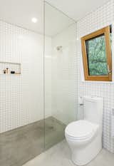Bath Room, Porcelain Tile Wall, Concrete Floor, One Piece Toilet, Open Shower, Recessed Lighting, and Corner Shower The bathrooms feature simple white tiles with concrete floors, while pocket doors throughout the home are painted in primary colors to create a subtle pop of bright color. 

  My Saves from A Bright Yellow Reading Nook Steals the Show in This Energy-Efficient Portland Abode