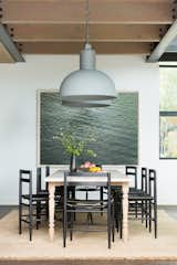 The dining room table is a new, custom-made piece from Nickey Kehoe. It is paired with ebonized black wood chairs with leather sling style seats by Sawkille Co. The chunky braided jute rug with fringe is from Armadillo & Co., the large pendant lights are from Frezoli Lozz, and the artwork is a photograph by Richard Misrach. 