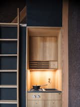 Kitchen, Wood Counter, Wood Backsplashe, Wood Cabinet, Cooktops, Undermount Sink, and Accent Lighting The A45 is outfitted with a petite kitchen designed by Københavns Møbelsnedkeri. 

  Photo 6 of 10 in This Sleek, Angular Tiny Home Is Not Your Average A-Frame Cabin