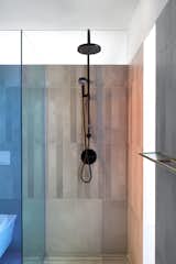 Bath Room, Concrete Wall, Open Shower, Concrete Floor, and One Piece Toilet The dichroic glass displays two different colors by undergoing a color change in certain lighting conditions. The concrete tiles reference the Brutalist building. 

  Photo 16 of 18 in An Iconic T-Shaped Apartment Receives a Modern Makeover