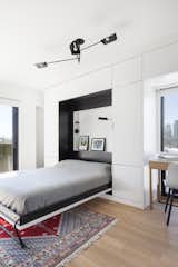 Bedroom, Light Hardwood Floor, Chair, Bed, Rug Floor, Pendant Lighting, Storage, and Wall Lighting The hideaway bed tucks neatly into the storage unit.  Photo 10 of 18 in An Iconic T-Shaped Apartment Receives a Modern Makeover
