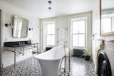 A beautifully designed, light-filled bathroom features a deep Victoria + Albert freestanding tub, an original marble mantle, a large black marble-topped vanity, and an encaustic concrete-tiled floor.&nbsp;