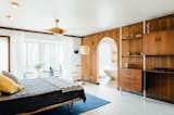 Bedroom, Ceiling Lighting, Rug Floor, Shelves, Bed, Porcelain Tile Floor, Bookcase, Chair, and Wall Lighting An arched doorway leads to an ensuite master bath.  Photo 8 of 12 in A Midcentury Gem in Utah Is Listed For $550K