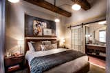 Exposed wood beams are set against contemporary artwork and custom furniture in this bedroom. An expansive modern chandelier, finished in black, provides ample downlighting for the large room.&nbsp;