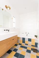Myers brightened up the bathroom with an assortment of tiles and a floating wood vanity. Cle Tile's farmhouse brick wall tiles line the tub, backsplash, and shower. The floor is a fresh and random mix of 8" square solid cement floor tile in Federal Blue, Ash, and Curry.