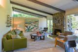 Classic midcentury features like the wall of glass and clerestory windows provide the home with a connection to the outdoors and flood the living space with natural light. A rough stone-inlay fireplace connects the living room with the facade.