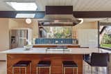 The updated kitchen of this circa-1969 Claude Oakland-designed Eichler has walnut-paneled cabinetry, quartz countertops, a turquoise tile backsplash, and a large center island with seating.
