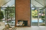 A bold wood-burning brick fireplace framed by glass anchors the open-plan living space. 