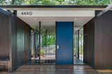 Framed by floor-to-ceiling glass, the bright blue front door adds a pop of color to the facade.
