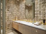 Tiny gold tiles wrap the countertop and play off graphic 1960s wallpaper in one of the home’s five bathrooms.