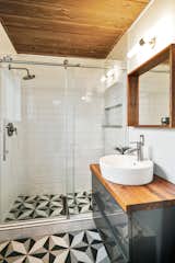 The bathroom has been updated with graphic tiles and a modern vanity that ties in with the wood-paneled ceiling.&nbsp;