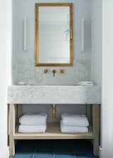 The bathroom is a mix of marble and brass with a custom vanity. 