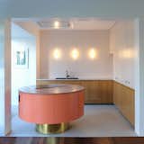 Otten opened the kitchen of this midcentury home in the suburbs of Antwerp and inserted a custom-made kitchen island with a pink concrete countertop and electric cooktop range. Pastel shades paired with wood and brass make the salmon-colored island pop.&nbsp;