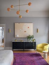Allied Maker Court Sconces pick up brassy tones from the lighting and highlight a peach-toned, abstract painting from Jen Winks Hays. A pair of vintage Milo Baughman barrel chairs further brighten the space with their sunny shade of yellow.    