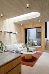 There are many textures at play in the living room—the board-formed concrete ceiling, the light brick wall, wood paneling, and the terrazzo floors. "The texture of the timber is reflected in the concrete," says Peake. The lightwell adds an additional internal light source and another spot to insert greenery. The Vibia Palma wall sconce from Koda Lighting is affixed to the wall over the sofa.