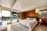 The main bedroom has glass sliding doors that lead out to the pool patio. There are warm wood walls, a period-appropriate Nelson cigar wall sconce, and an ensuite bathroom.&nbsp;