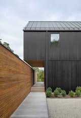 The black-stained gable cantilevers over the entryway and aligns flush with the landscape wall, creating a horizontal gap that intersects with the vertical space between both walls. 