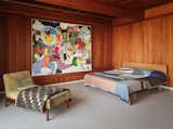 The bedroom features an original Gerald Luss chaise for Lehigh Furniture Company from the 1950s. Hanging on the wall is a work by Eddie Martinez, "Ideal Location" (2021). The bedspread, titled "Botanic Study - Indigo," is by Kiva Motnyk (2021).