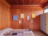 Another wood-paneled bedroom features hanging works. From left to right: "Scene of Elapsing Connections" by Kishio Suga (2009); "Wooden Spaces in Alignment" (2001); "Continuous Earth Under Rain" (2009); "Point of Centrality" (2000); "Potential Detachment" (2007); "Cluster of Rising Sceneries" (1997); "Internal Boundary in Formation" (2010). The bedspread by Kiva Motnyk is titled "Line Tapestry - Neutral" (2021).