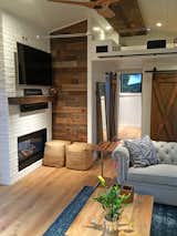 Living room and door to master bedroom, Chesterfield sofa, double-sided fireplace, reclaimed wood mantle piece, television, and reclaimed wood wall accent. Storage loft.