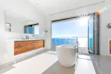 Like an illusion, this minimal oceanside bathroom bounces off the natural light seeping through a NanaWall system. A large bathtub has been strategically situated in front of the folding glass wall for the ultimate relaxation experience accompanied by the sound of crashing waves and refreshing ocean breeze.