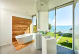 The minimal features of this bathroom are accentuated by the minimal features of the NanaWall minimal sliding glass system. Three large floor to ceiling glass panels eloquently frame endless ocean views and provide easy egress to the bathtub after a long day at the beach.