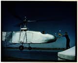 Left side view from slightly forward of Sikorsky VS-300A in low-level hovering flight, piloted by test pilot Les Morris; an unidentified man places a bundle in the helicopter's nose basket; 1943.  Photo: Hans Groenhoff, Smithsonian National Air and Space Museum.