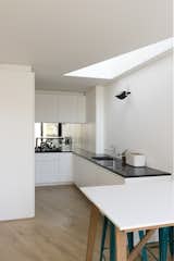 The kitchen space is defined by the overlapping intersection of a rectilinear volume and a triangular roof-light, while a mirror visually extends the new architecture into the existing building.