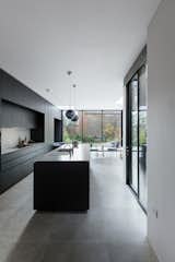The handleless black kitchen units are articulated as rectilinear sculptural elements, at the same scale as the white volumes and planes that loosely divide the open plan spaces. The kitchen and dining space are surrounded by courtyard gardens on two sides.