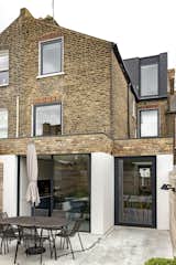Separated by glazing, the exterior of the rear extension is articulated as two vertical planes of white render, and two horizontal planes of brick, while the roof extension is composed of two vertical planes of slate.