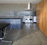 The downstairs communal living spaces flow freely between kitchen, dining room, and living room. Concrete block walls and polished concrete floors emphasize the heavy materiality that supports the visual lightness of the upper story.