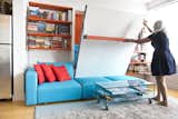 Annette demonstrates the ease of lowering the Swing, a queen-size wall bed with nine-foot sofa and sliding chaise. Here, it integrates with a shelving system, which continues the apartment's quirky motif of orange and blue.  Photo 4 of 6 in Two Film Industry Veterans Flip the Script With a Suburb-to-City Move