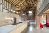 David Nossiter Architects transformed a crumbling barn complex in Sussex, England, into a full-time residence comprised of farm buildings laid out in a cruciform plan with a courtyard in the middle. With cathedral-like proportions, the converted building is complete with exposed brick walls and wood rafters from the original structure. The concrete worktops and sinks in the minimalist kitchen were designed by the homeowners.