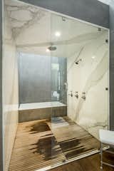 A deep soaking tub complements a shower lined with marble and wooden slats. A double vanity sits opposite.