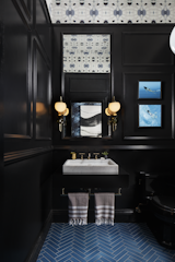 Designed by Benni Amadi Interiors and Courtney Springer Interiors, the "Moody Blues" powder room and vestibule pairs a marble sink with dramatic black walls that make the room seem more spacious, while blue tiles laid in a herringbone pattern reference the traditional architecture of &nbsp;the home.