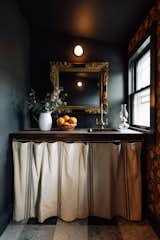 Connected to the private dining room is a small bar, which used to be part of the public bathrooms on the ground floor. William Morris wallpaper and a brass faucet from Signature Hardware create contrast against the moody paint. The wall sconce is by In Common With.
