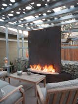 Shimmer and rust. The shade structure was galvanized off site and assembled here over the patio. A sister structure covers a dining patio toward the rear of the garden. Laser-cut panels leave circles of light on the ground and adjacent walls. 

The fire feature is a linear burner faced with corten steel. The upright steel reflects heat back on to guests seated in an outdoor lounge. 

Planting is minimalist: sedges and rushes, and whatever else can resist the dogs.
