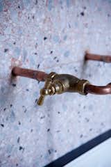 Copper piping extends out from the wall to become the faucets in a terrazzo-covered bathroom in Paris, France.
