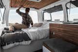 Cargo Van Mobile Studio bedroom with repurposed wood accents, Zach Both shown grabbing books from small shelf over bed