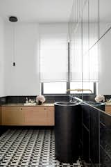Another bathroom boasts a striking black-and-white patterned tile on the floor and is completed with gold faucets, wooden cabinetry, as well as a contemporary black sink.