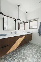 The master bathroom features cement tile with a wall hung, walnut vanity with a white quartz counter top. Rounded edge, square mirrors and matte black pendant lights finish off the look
