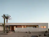 Front elevation at twilight of desert modern new home in Phoenix Arizona featuring breeze block, wood slats, date palm tree aperture, and pocketing sliding glass doors