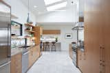 Light floods the kitchen through multiple skylights and a backsplash window, and vertical grain fir cabinets and floating shelves accent the neutral palette.