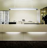 The linear T-Light Pendant features parallel pieces of extruded aluminum that hang from two stems and sandwich a ¾” thick piece of etched, water white glass and form an upside down “T”. Two strips of 3000˚K LEDs provide warm up and down-light and are wired as dual circuits, which allows each light source to be dimmed separately. Once hung, each of the two stems can be adjusted independently to level the pendant. The T-Light comes in a myriad of standard powder coat finish options:  Cinnamon Bronze; Rubbed Bronze; Silver Fog; Black Granite; Gossamer Aluminum; Gloss White; Golden Gate Orange; and Coffee Bean. 12 specialty powder coat options available. Available in 5’, 6’ and 7’ lengths. #lighting #commerciallighting #pendant #LED #office #officelighting #architecturallighting #frontdesk #receptiondesk