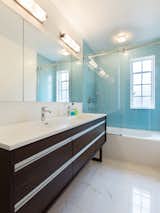 Blue glass tile anchors the compact family bathroom with custom ebony vanity with a trough sink by Wetstyle