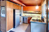 The kitchen in this home features its original cabinets, stainless-steel countertop with integrated sink. and tile backsplash. a new section of stainless-steel countertop was added on the right to replace the original range and clothes-washing machine.