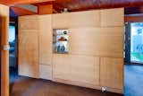 This wood paneled room divider separates the kitchen from the living room, and is a piece of millwork, rather than a wall. The design, including the architectural glass penetration with display shelves, is as originally built.