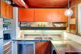The kitchen in this home features its original cabinets, stainless-steel countertop with integrated sink. and tile backsplash. a new section of stainless-steel countertop was added on the right to replace the original range and clothes-washing machine.